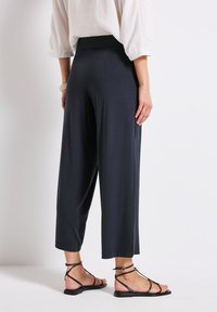 Navy culottes with a wide leg design and elastic waistband, paired with black strappy sandals, featuring a smooth textured fabric.