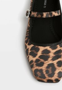 Chaussure plate marron et noire à imprimé léopard, avec un bout carré et une fine bride de cheville avec une boucle argentée.
