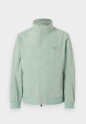 Veste zippée vert clair avec col montant, manches élastiques, poches latérales zippées et logo "Porsche BOSS" sur la poitrine.