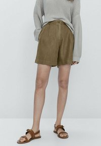 Brown linen shorts with pleats, featuring a front button closure and side pockets, paired with a gray knit sweater and brown sandals.