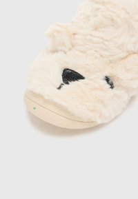 Pantofole morbide di colore crema con dettagli neri che ricordano il muso di un orso, punta rotonda e suola testurizzata beige con delle macchie.
