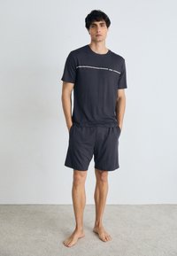Tricou scurt gri închis cu mânecă scurtă, având o dungi contrastante deschise și un logo, asociat cu pantaloni scurți asortați, ambele dintr-un material moale și fin.