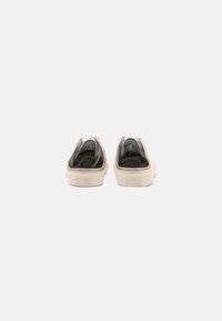 Scarpe slip-on in tela beige con accenti neri, dotate di punta rotonda, suola in gomma testurizzata e logo impresso sul tallone.
