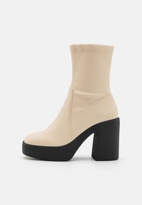 Bottines beiges à tige extensible, talon épais noir texturé et semelle plateforme. Caractéristiques d'une couture minimale et d'un design épuré.