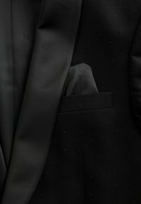 Jachetă de tuxedo neagră cu rever din satin neted, țesătură texturată cu puncte subtile și un batiste pus în buzunarul de la piept.