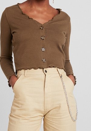 Bruine geribbelde, geknoopte cropped top gecombineerd met beige, hoogtaile broeken met een zilveren ketting aan de zak.