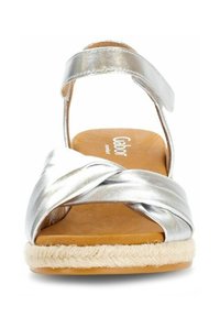 Silberne, metallische Sandale mit einer geflochtenen Espadrille-Sohle, ausgestattet mit überkreuzten Riemen und einem hinteren Knöchelriemen für zusätzlichen Halt.