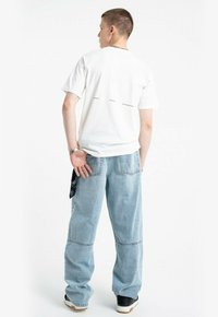 Biały bawełniany t-shirt z krótkimi rękawami, z nadrukowanym tekstem z tyłu. Jasnoniebieskie, luźne dżinsy z boczną kieszenią. Czarne trampki.