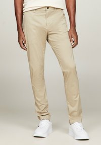 Chino beige a taglio slim, realizzati in morbido tessuto di cotone. Presentano una chiusura con bottone frontale e tasche laterali. Abbinati a sneakers bianche.