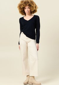 Svart stickad tröja med V-ringning och spetsstickade ärmar, tillsammans med högmidjade, beige vida byxor och beige ankelskor.