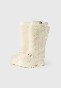 Chlupaté kotníkové boty v krémové barvě, s tlustou podešví, stříbrnou sponou a měkkou texturou pro zvýšení vizuálního zajímavosti.