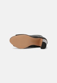 Chaussure en cuir noir perforé vue de la semelle, avec une semelle lisse couleur fauve et un petit talon épais.