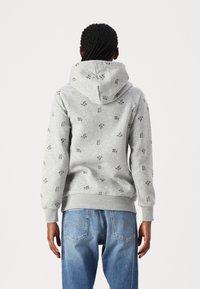 Grey hoodie with a drawstring, featuring small black leaf patterns. It has a kangaroo pocket and ribbed cuffs, worn with light blue jeans.