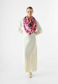 Écharpe en soie avec un motif floral dans des nuances de rose, violet et rouge, portée de manière décontractée sur une robe en satin crème à manches longues.