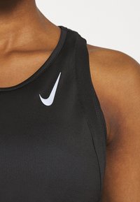 Czarna sportowa koszulka bez rękawów z okrągłym dekoltem, teksturowana tkanina oraz białym logo Nike w kształcie swobody na górnej lewej części klatki piersiowej.