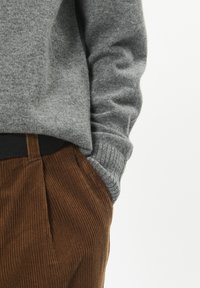 Pulover gri tricotat cu manșete cu nervuri, purtat cu pantaloni din catifea cord cu dungi verticale și un brâu negru.