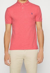 Rotes Polohemd aus Baumwollmischung, mit einem kragenähnlichen Ausschnitt, zwei Knöpfen und einem kleinen blauen Logo auf der linken Brust.