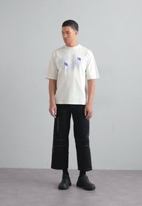 Cremefarvet t-shirt med korte ærmer og grafisk tryk, sat sammen med sorte cropped bukser med hvid syning. Sorte chunky sko fuldender looket.