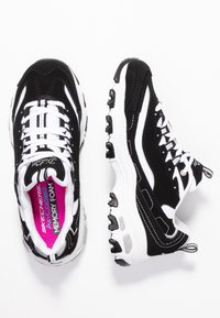 Svarta och vita träningsskor med ett texturerat tygöverdrag, synliga snören och en dämpad sula med accenter och logodetaljer.