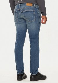 Vaqueros de mezclilla azul oscuro con corte ajustado, que presentan una cintura de altura media, cinco bolsillos y un ligero efecto desgastado. Combinados con zapatillas negras.