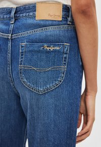 Μπλε τζιν παντελόνι από ντένιμ με ελαφρύ ξεβάφτισμα, με δερμάτινο ταμπελάκι που φέρει την ένδειξη "Pepe Jeans" και χρυσαφί ραφές στην πίσω τσέπη.