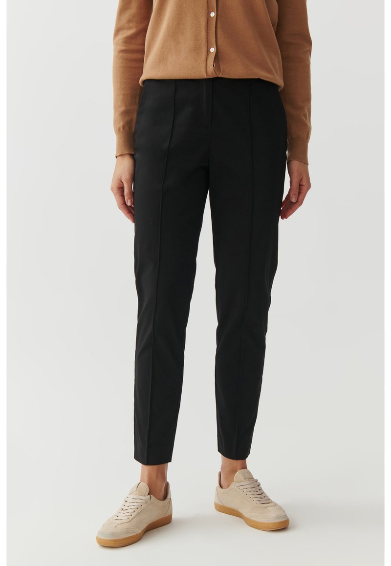 Zwarte tailleurbroek met een slim fit, voorzien van voorkantnaden en een gladde textuur, gecombineerd met lichtbeige sneakers.