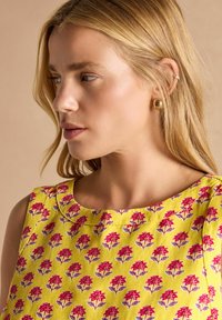 Kollane kleit roosa ja lilla lillemustriga. Sile kangas, ümmargune kaelus, ilma varrukateta. Kuldsed ruudukujulised kõrvarõngad.