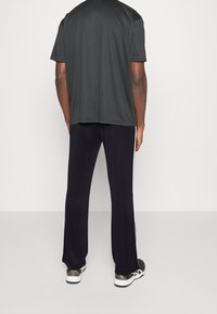 Černé síťované tričko s krátkými rukávy a volným střihem; v kombinaci s černými kalhotami s bílými bočními proužky. Tenisky s vzorovanými akcenty.