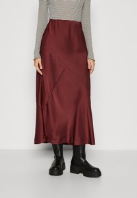 Fustă maxi din satin burgund cu cusături diagonale, textură netedă și siluetă evazată, asortată cu ghete negre masive până la gleznă.
