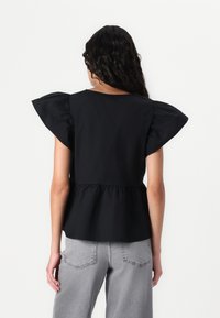 Svart peplumtop med puffärmar, slät textur, rund halsringning och avslappnad passform; ihop med ljusgrå vida jeans.