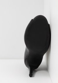 Chaussure à talon haut noire avec une tige en cuir lisse et épuré, et un bout pointu. Semelle en caoutchouc texturé avec un talon aiguille fin.