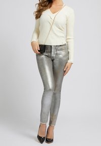 Metaliczne srebrne dżinsy o slim fit i wysokim stanie, w połączeniu z kremowym, prążkowanym, długim topem z rękawem oraz czarnymi szpilkami.
