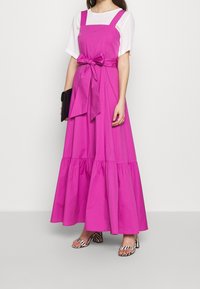 Fuksiansävyinen maksimekko säädettävillä hihnoilla, solmittavalla vyötäröllä ja kerroksellisella helmalla. Yhdistetty mustavalkoisiin raidoitettuihin lohkokorkoisiin sandaaleihin.