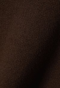 Gros plan d'un tissu tricoté marron foncé avec une texture côtelée verticale visible et une surface douce légèrement courbée.