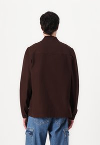 Brun langermet skjorte med klassisk krage, glatt tekstur og knappedette ermer, parret med lyseblå cargo-jeans.