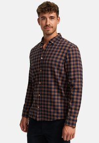 Brun og marineblå ternet skjorte med krave, lange ærmer og træknapper; stoffet ser blødt og tekstureret ud.