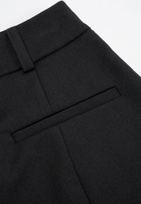 Zwarte broek van een gestructureerde geweven stof. De tailleband is glad, met een achterzak die is omlijst door een subtiele naaddetail.