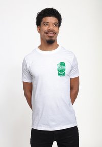 Hvid bomulds t-shirt med et grønt grafisk design på den øverste venstre side. Klassisk pasform med korte ærmer og rund hals.