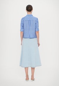 Camicetta a maniche corte a scacchi blu e bianchi con schiena arricciata, abbinata a una gonna A-line in denim blu chiaro con dettagli delle cuciture visibili.