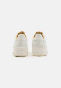 Baskets en cuir blanc avec une finition texturée, intérieur rembourré marron clair et logo blanc en relief sur la semelle. Design minimaliste et style basse.