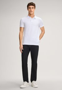 Wit poloshirt met een kraag, gemaakt van zacht katoen, gecombineerd met een donkere jeans en witte sneakers. Eenvoudig ontwerp, geen zichtbare patronen of logo's.