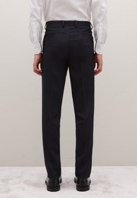 Marineblauwe op maat gemaakte broek met een rechte snit, voorzien van twee achterzakken en een gladde textuur, gecombineerd met zwarte schoenen.