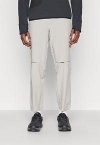 Világos bézs cargo nadrág több zsebbel, rugalmas derékrésszel, szűkítő lábformával, fekete sportcipővel párosítva.