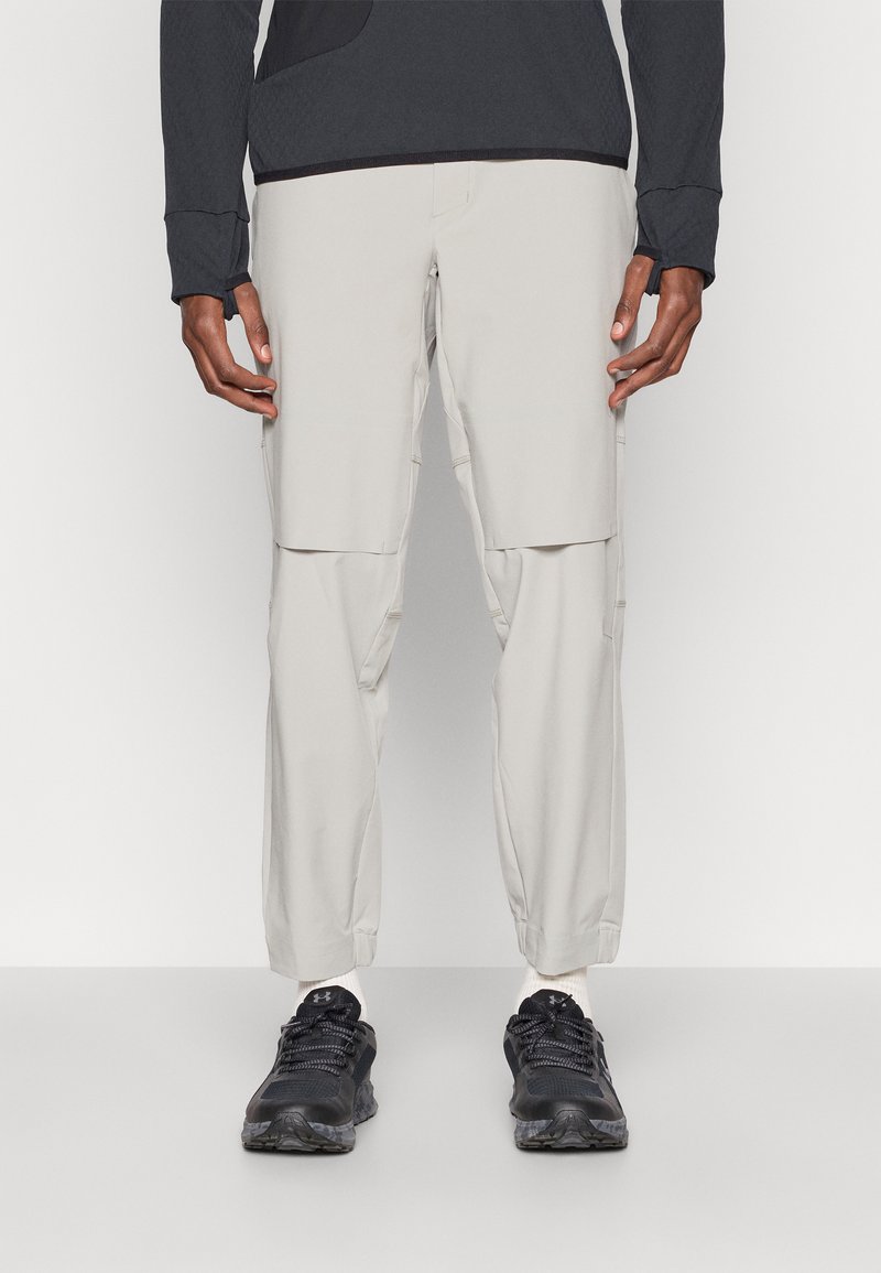 Világos bézs cargo nadrág több zsebbel, rugalmas derékrésszel, szűkítő lábformával, fekete sportcipővel párosítva.