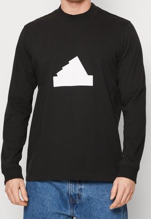 Chemise noire à manches longues en coton avec un design géométrique abstrait blanc présentant des formes angulaires sur le devant. Coupe décontractée et col rond.