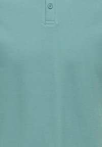 Polo texturé bleu sarcelle clair avec deux boutons sur la patte, en tissu respirant.