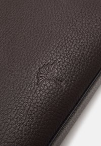 Portafoglio in pelle marrone scuro con una texture a granuli. Presenta un logo stampato, bordi lisci e un design minimalista.