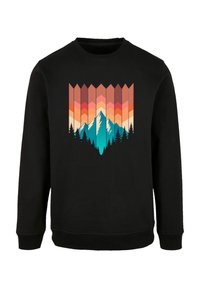 Schwarzer Pullover mit einem grafischen Design von Bergen und Bäumen in türkis, pink und orange, vor einem geometrischen Hintergrund.