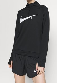 Mustapohja tutkimusalus, jossa on neljänneksen vetoketju ja valkoinen Nike-logo, yhdistettynä mustiin shortseihin, joissa on pieni valkoinen Nike-viiva.