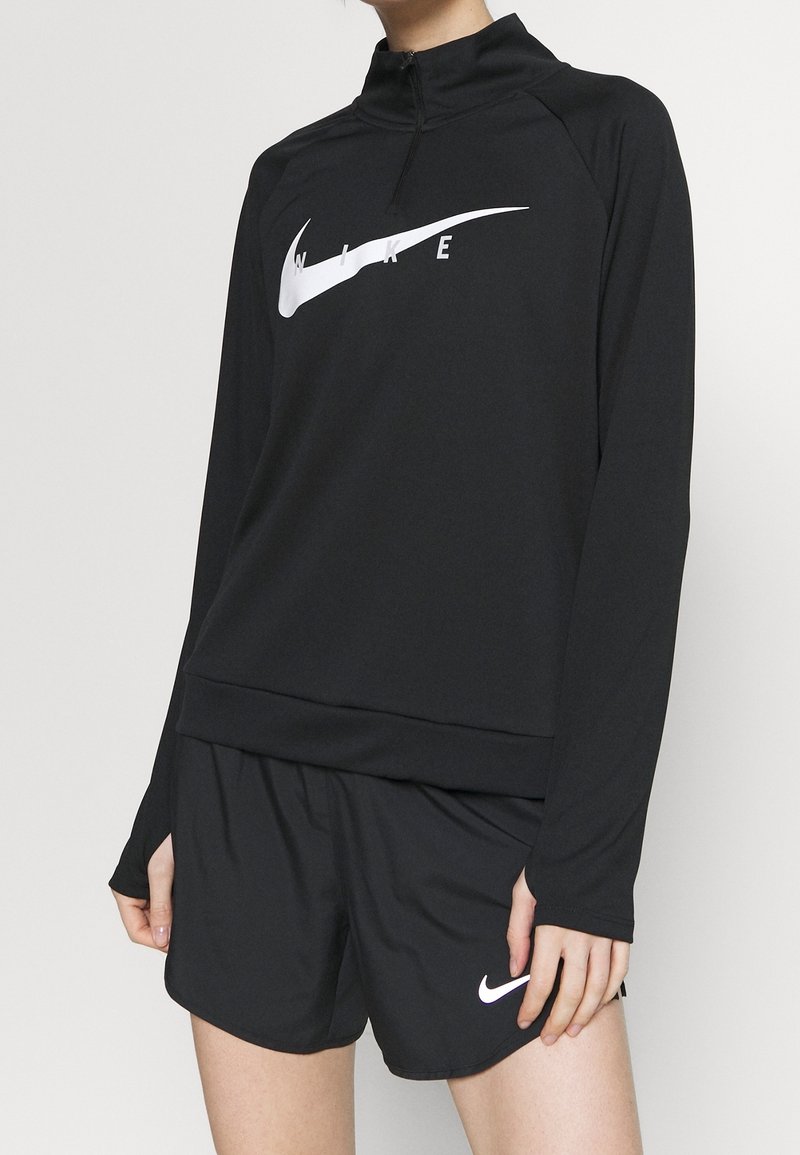 Černé sportovní mikina s čtvrtinovým zipem a bílým logem Nike, v kombinaci s černými šortkami s malým bílým logem Nike swoosh.